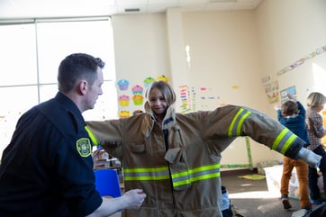 Firefighter helping young student try on fire jacket